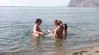 Three bare girls on the coast of a public beach without clothes