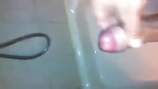 The kid caresses his dick with his hand in the shower stream